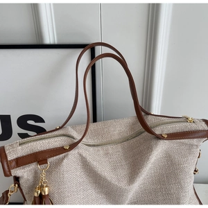 Detail of canvas tote bag featuring brown leather trim, gold zipper and tassel pendant