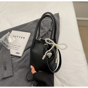 Sac seau noir chic avec nœud perlé et pendentif cœur sur une veste de blazer grise