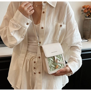Close-up of a small cream and green woven crossbody phone bag worn by a model