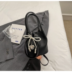 Détail du sac seau noir en cuir grainé avec nœud en perles et pendentif en cœur