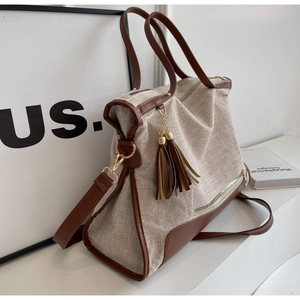 Detail shot of canvas tote featuring brown leather handles and a decorative tassel charm