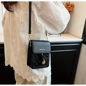 Detail of black woven crossbody phone bag with gold metal charm on white lace top