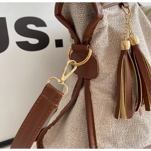 Detail of canvas bucket bag showing brown leather trim and golden metal hardware lock