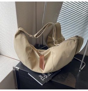 Detail view of beige crescent bag featuring adjustable strap and brown leather zipper puller