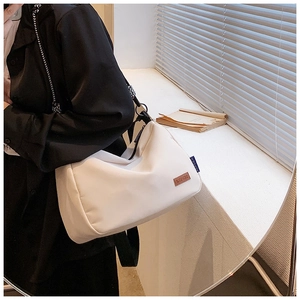 Détail de la sacoche en toile blanc cassé avec étiquette en cuir et bandoulière tissée noire
