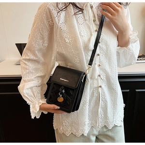 Detail of woven texture on a black crossbody phone bag with a gold metal pendant charm