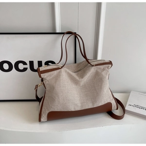 Detail of canvas tote bag with brown leather trim and detachable shoulder strap on a white stand