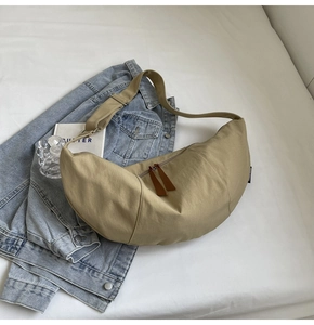Detail of khaki crescent crossbody bag with smooth zippers on white fabric background