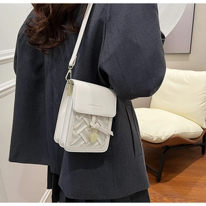 Close-up of woven cream white crossbody bag with metal charm and branded flap detail