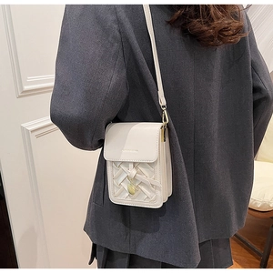 Detail of white woven square crossbody bag with round metal pendant and slim strap