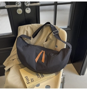 Detail of black crescent crossbody bag with orange leather pulls on beige trench coat