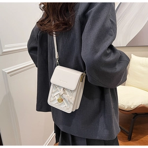Detail of woven white crossbody phone bag with metal charm on a female model