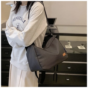 Détail du sac géométrique en toile noire avec sangle rayée et patch logo en cuir