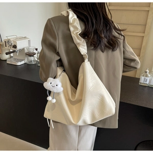 Chic cream tote bag with ruffled shoulder strap and plush cloud charm in cafe setting