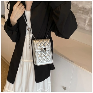 Close-up of silver quilted phone bag with heart lock and chain strap on model