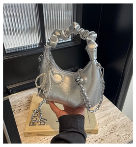 Détail d'un sac argenté effet métallisé avec pendentif perle et bandoulière en chaîne