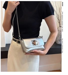 Detail of silver square crossbody bag with star clasp and chain strap on a model
