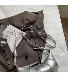 Détail du sac croissant argenté avec bandoulière nouée sur linge blanc doux