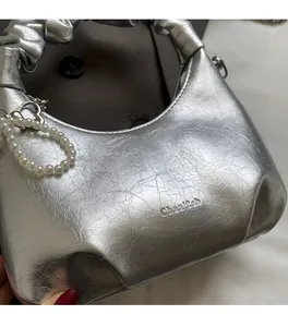 Detail of silver metallic wrinkled leather handbag with pearl charm and textured handle