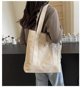 Detail of cream canvas tote bag featuring wide shoulder strap and front snap pocket