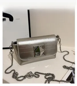 Detail of silver chain bag featuring a textured flap and large gold pyramid lock