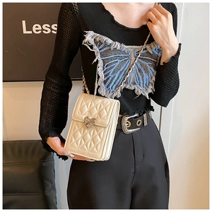 Detail of cream quilted crossbody bag with golden heart buckle and chain strap worn by model