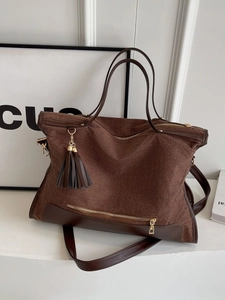Brown woven canvas tote bag with contrast leather trim and decorative tassel pendant
