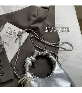Detail of silver pleated crescent bag with pearl charm and metal chain strap on brown suit