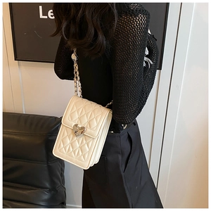 Model wearing a quilted crossbody bag with heart-shaped buckle and chain strap