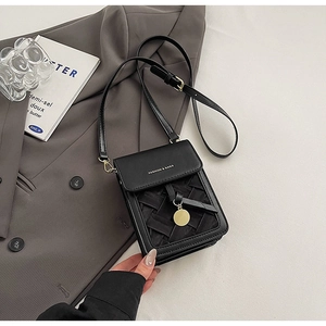 Detail of black woven leather crossbody bag with gold charm on a grey blazer