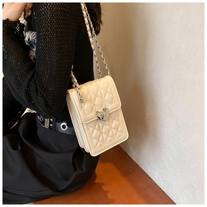Detail of ivory quilted crossbody bag with silver heart clasp and chain strap