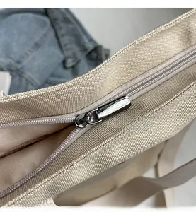 Close-up of a smooth silver metal zipper on a durable beige canvas tote bag detail