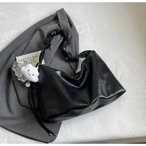 Detail of black pleated leather tote bag with cloud charm on grey suit background