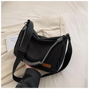 Détail d'un sac bandoulière en toile noire avec poignée tressée et logo en cuir