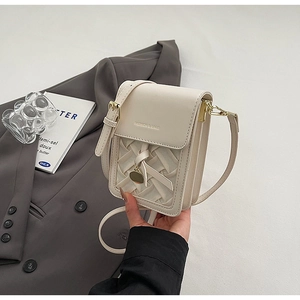 Detail of cream white small crossbody bag with woven texture and gold charm on a suit