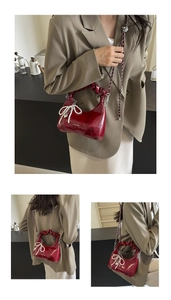 Detail of dark red patent leather bag with pearl bow, heart charm and silver chain strap