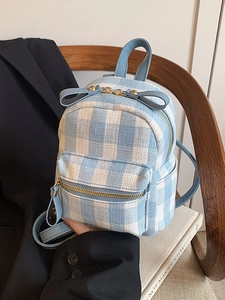 Mini blue and white plaid tweed backpack with bow detail and gold hardware on chair