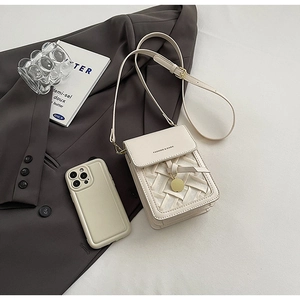 Detail of cream crossbody bag featuring woven texture flap and golden round pendant