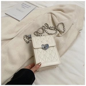 Detailed view of white quilted crossbody bag with heart-shaped metal lock on fabric