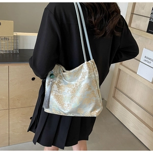 Detail of light blue embroidered tote bag with gold landscape patterns and tassel