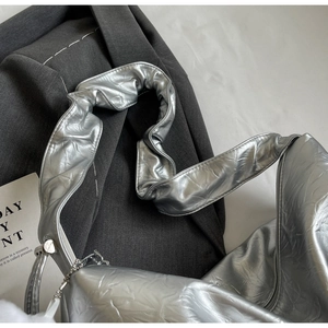 Detail of silver pleated tote bag with soft pompom charm and metal chain on grey blazer