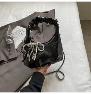 Détail d'un sac à main noir brillant plissé avec nœud en perles et chaîne argentée
