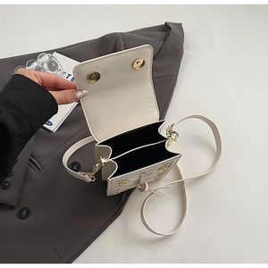 Detail view of the beige quilted mini crossbody bag with heart charms and dual compartments