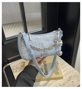 Détail du sac tressé bleu clair avec chaîne argentée et breloque nœud sur marbre