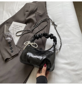 Détail du sac bandoulière plissé noir avec breloque nœud perlé et chaîne en métal