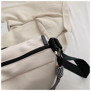 Détail du sac en toile blanc cassé avec fermeture éclair noire et nœud décoratif tissé