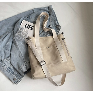 Detail of beige canvas tote bag with front snap pocket and dual straps shown in flat lay