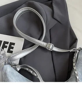 Detail of adjustable silver shoulder strap with metal buckle and decorative chain on denim bag
