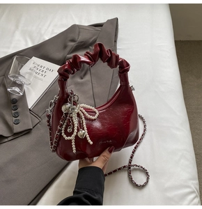 Détail du sac à main plissé bordeaux avec nœud en perles et breloque cœur sur blazer