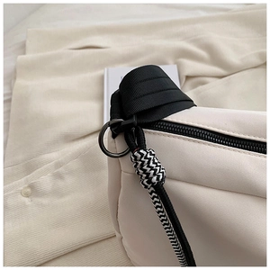 Gros plan sur la fermeture éclair noire et la large bandoulière en nylon du sac beige
